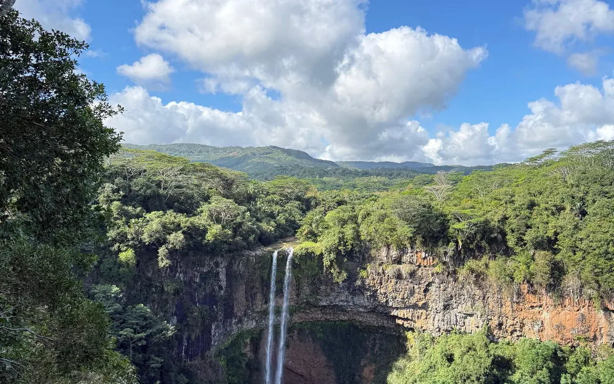 Twin streams of the Chamarel falls dropping from a basalt cliff into a forested gorge, with green hills behind