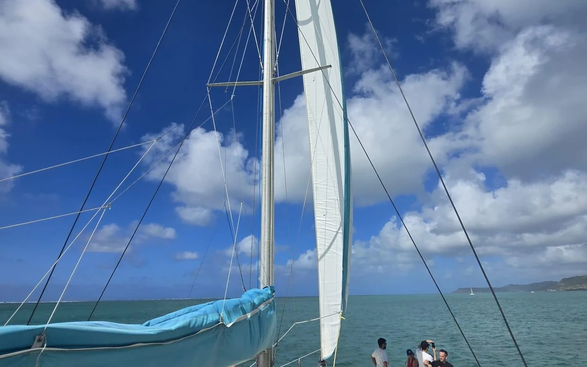 La vista dal ponte di un catamarano sotto una vela bianca issata, con la laguna turchese e la costa all'orizzonte